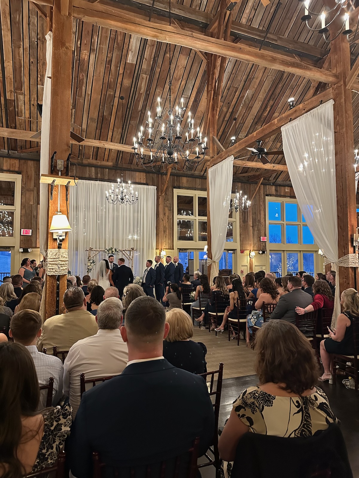 Rustic barn wedding ceremony with chandeliers and wooden beams